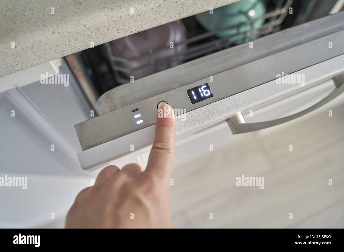 Female hand pressing button on modern dishwasher control panel in kitchen setting Stock Photo