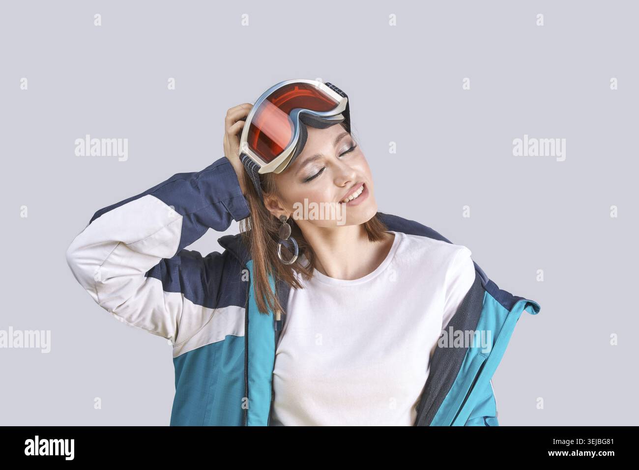 Young caucasian female wearing ski jacket and goggles in relaxed pose on gray background Stock Photo