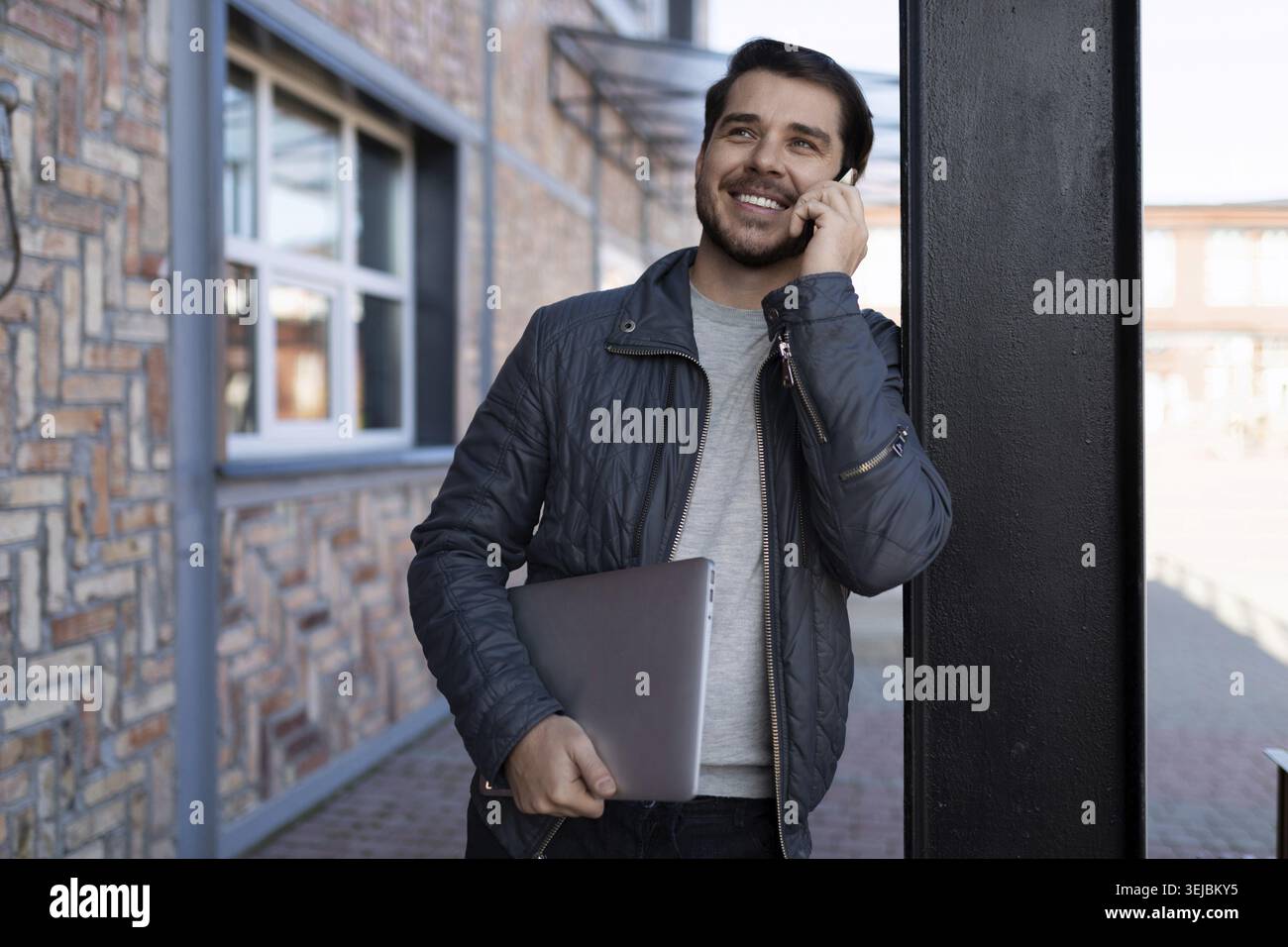Middle-aged man programmer talking on a mobile phone with a laptop in his hands Stock Photo