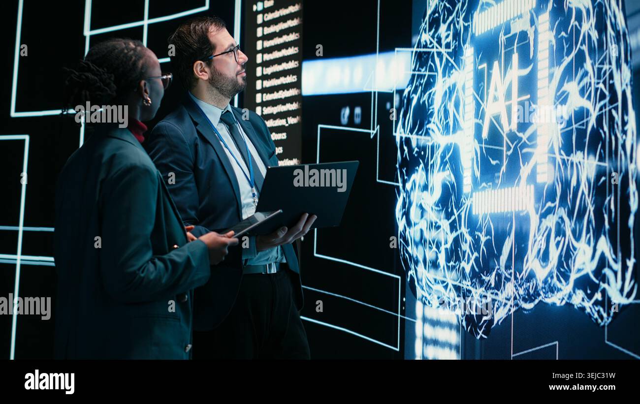 Engineering team looks at AI machine learning self writing code on screen, autonomy concept. Teamworking colleagues reviewing self sustaining artificial intelligence model, doing brainstorming Stock Photo
