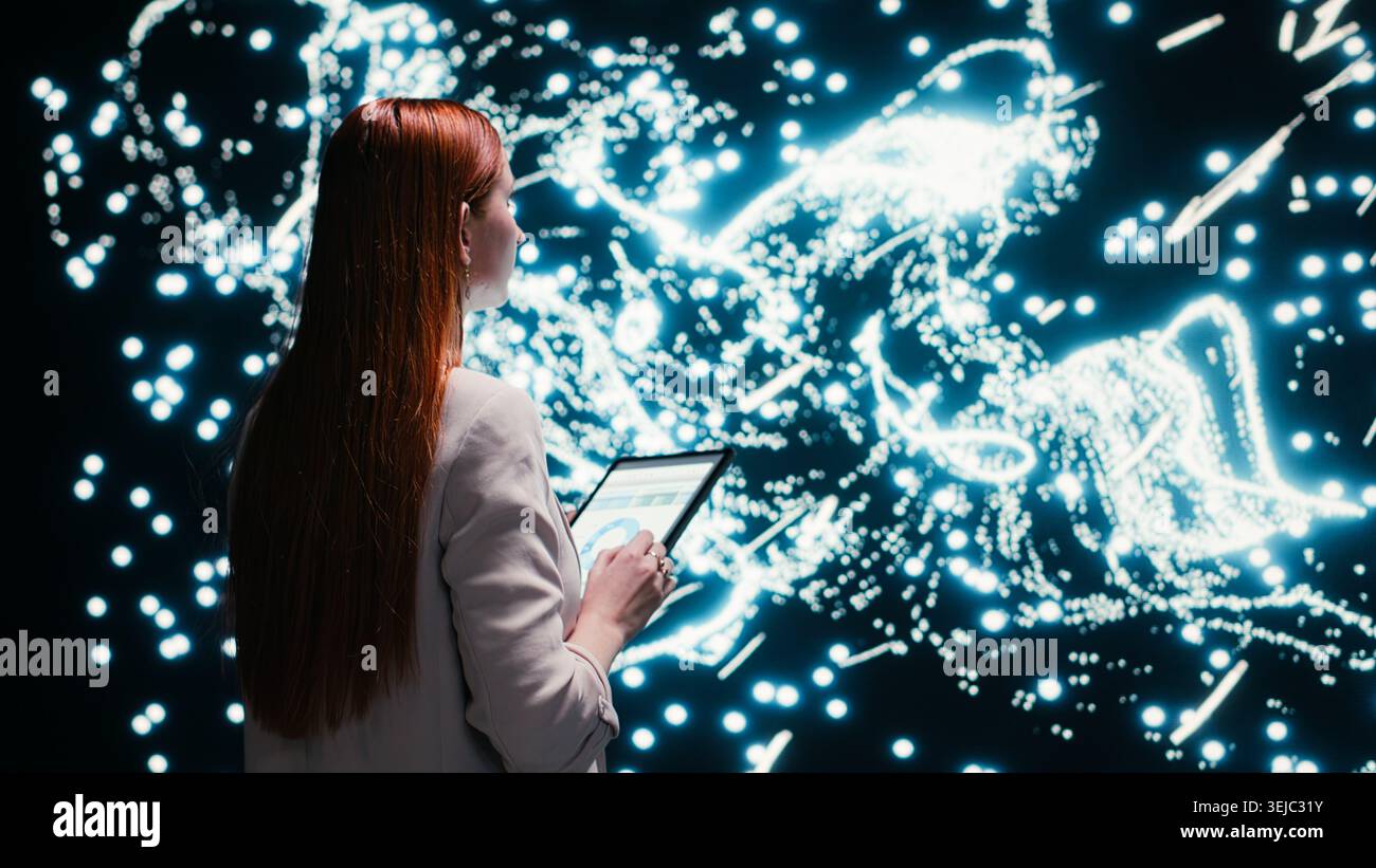 Software developer optimizes neural network neurons map with tablet and augmented reality tech. Female technician fine tuning AI model synaptic weights with touchscreen device, camera B Stock Photo