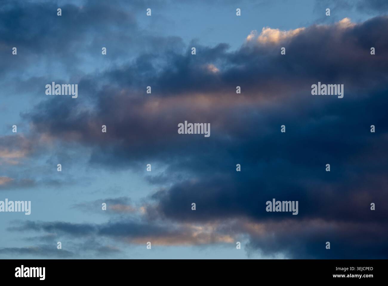 Dark brooding clouds with subtle warm tones against a pale blue sky Stock Photo