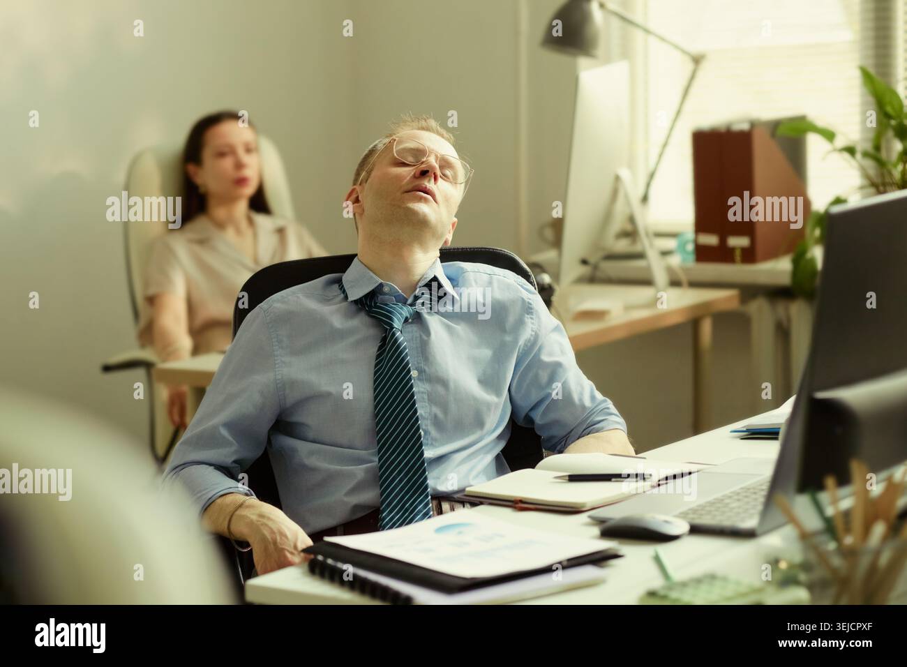 Middle aged Caucasian businessman leaning back with closed eyes at desk, feeling exhausted during office work. Suitable for burnout, workplace stress, fatigue awareness campaigns Stock Photo