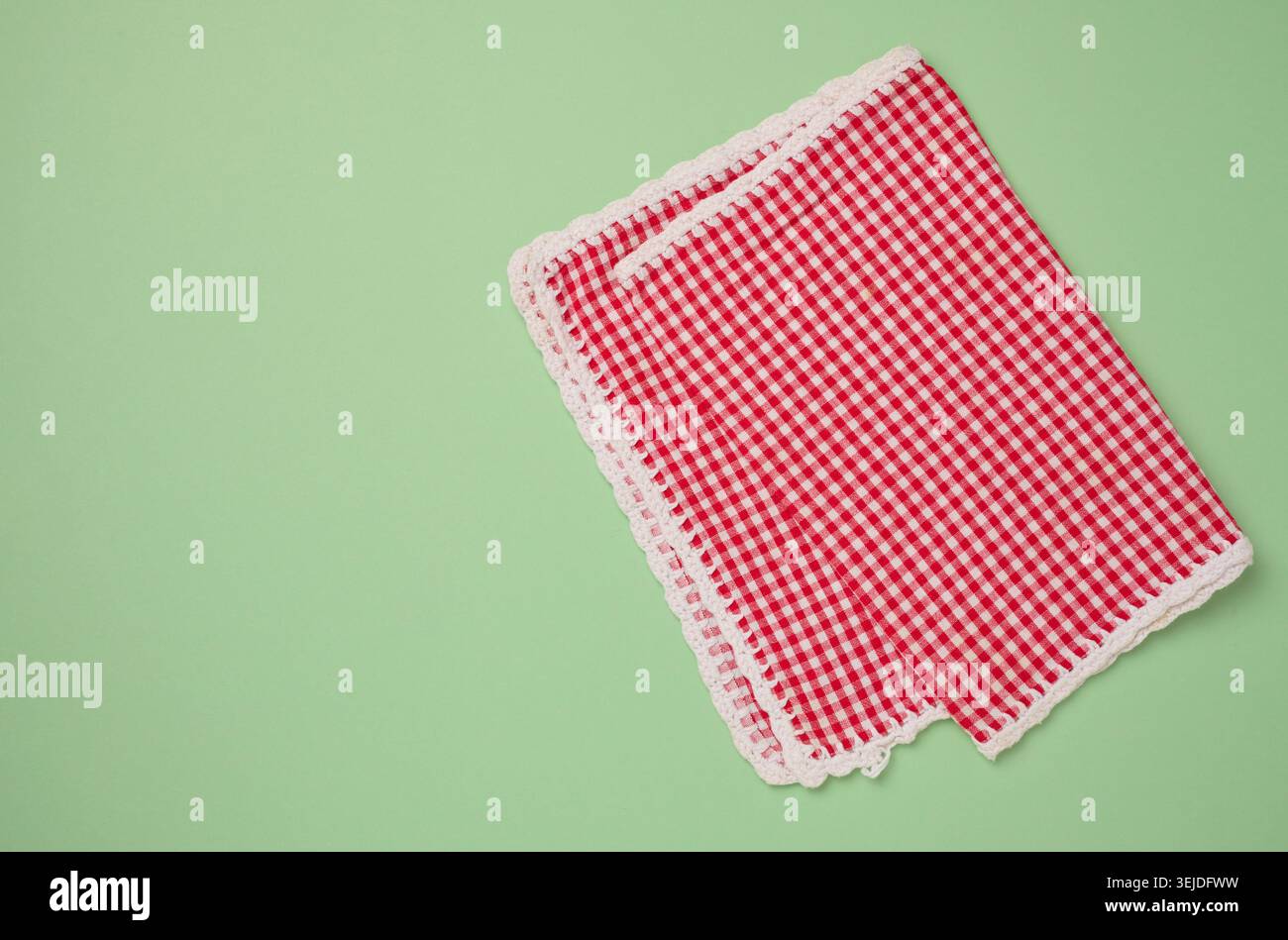 Folded red kitchen towel on a green background, top view. Stock Photo