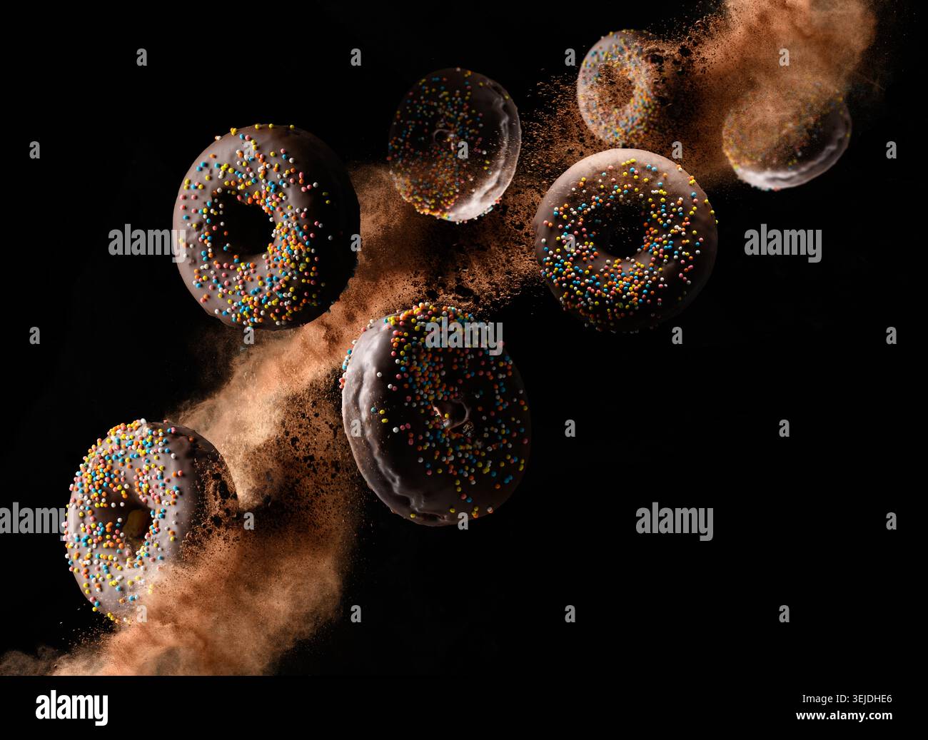 Chocolate donuts with colorful sprinkles levitate on a black background with loose cocoa Stock Photo