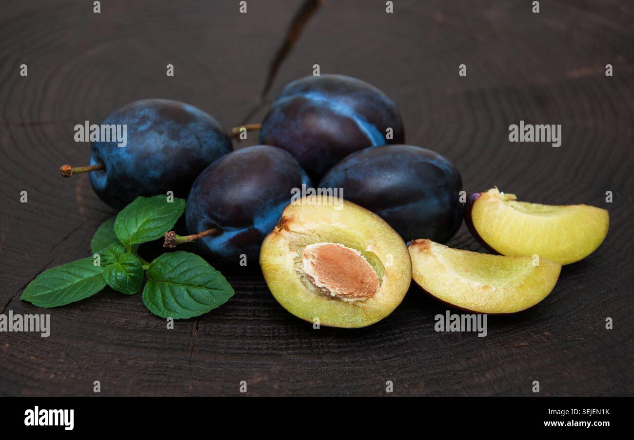 Fresh plums with green leaves on a old black wooden background Stock Photo