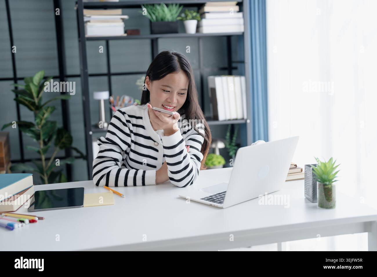 Asian Woman Engaging with Voice Assistant on Smartphone in Modern Home Stock Photo
