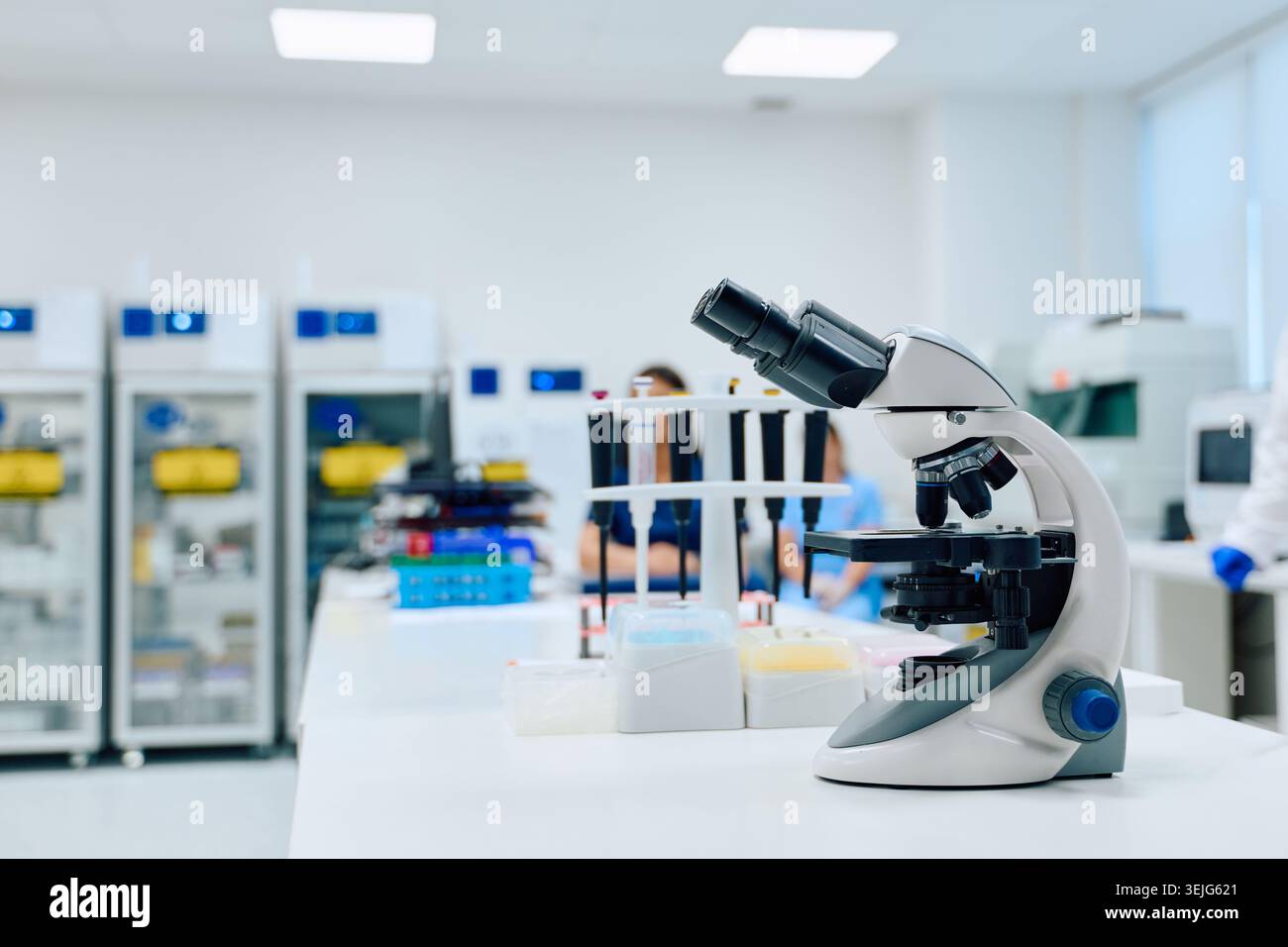 Microscope in a modern laboratory with scientists conducting research during daylight hours Stock Photo