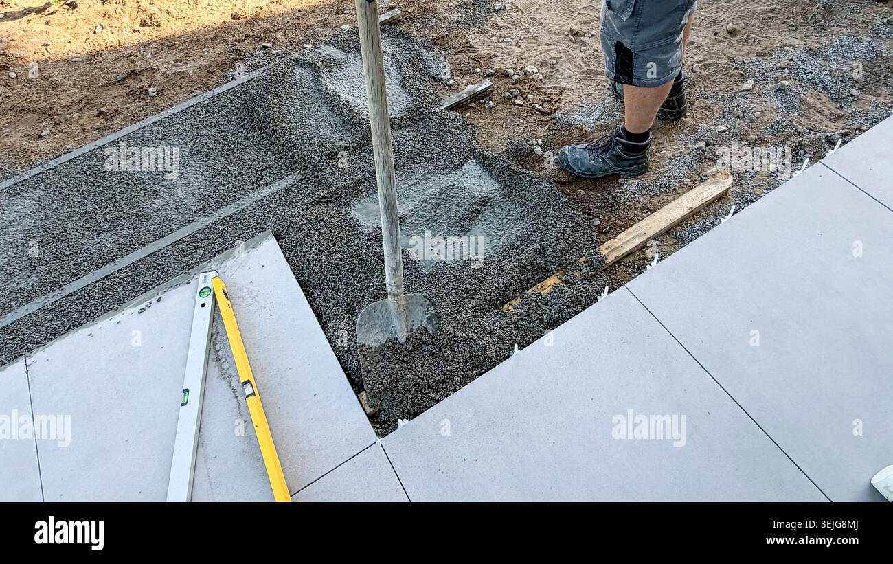 Construction worker using a concrete vibrator to level freshly poured concrete on a construction site with tools and gravel visible in the background Stock Photo