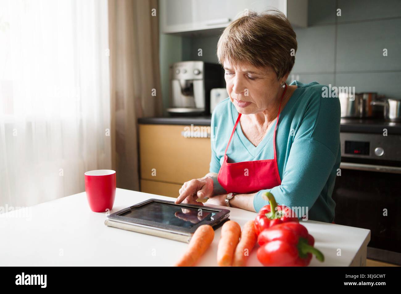 Elegant elderly woman using  tablet in the kitchen Stock Photo