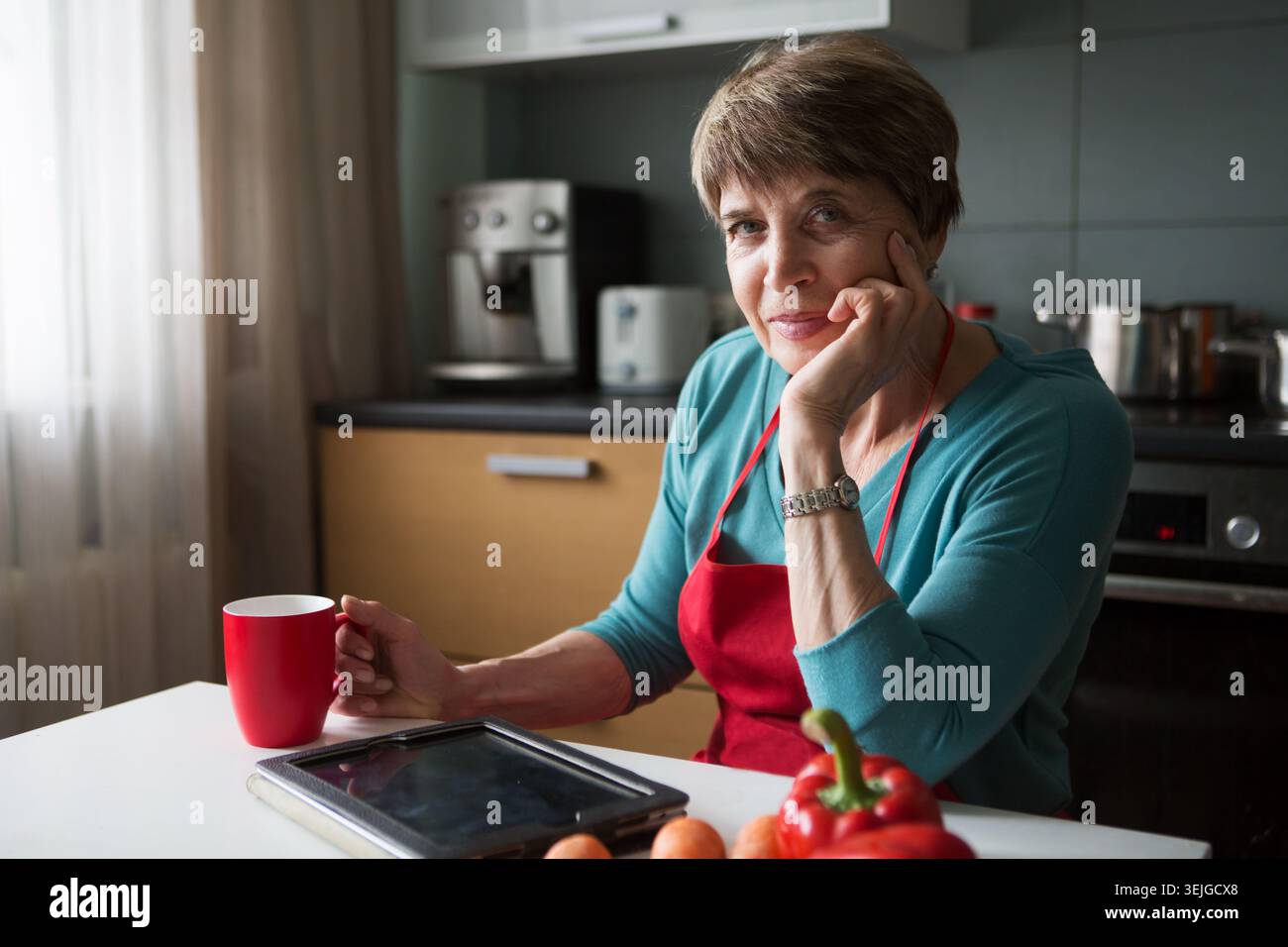 Elegant elderly woman using  tablet in the kitchen Stock Photo