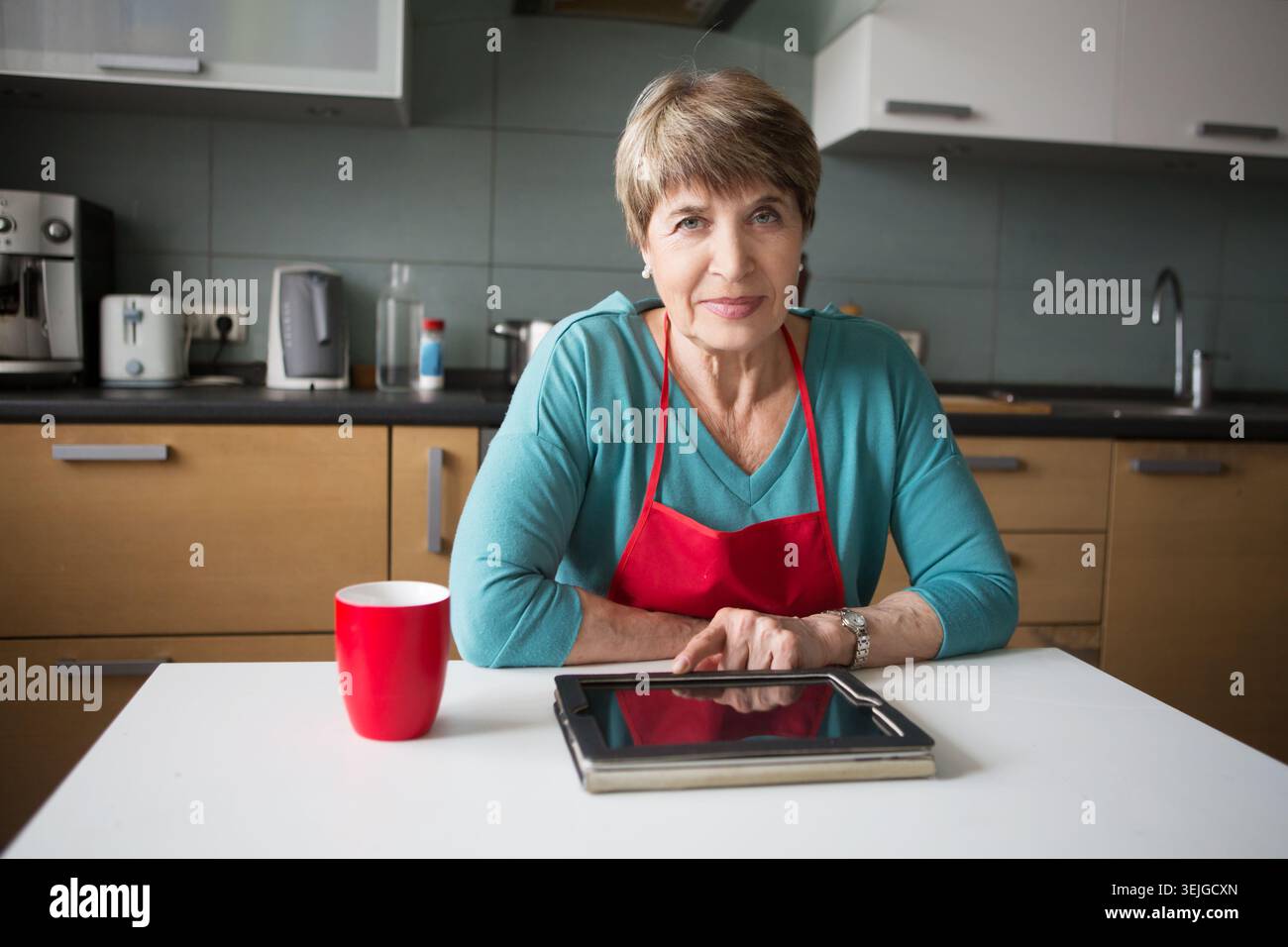 Elegant elderly woman using  tablet in the kitchen Stock Photo