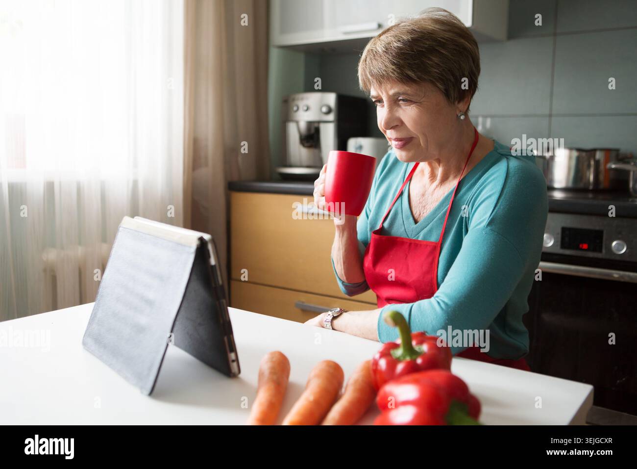 Elegant elderly woman using  tablet in the kitchen Stock Photo