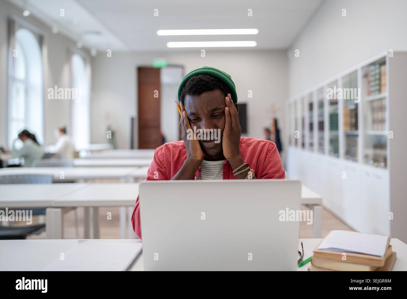 Stressed tired african american student guy tired of learning sitting in library looking at laptop Stock Photo