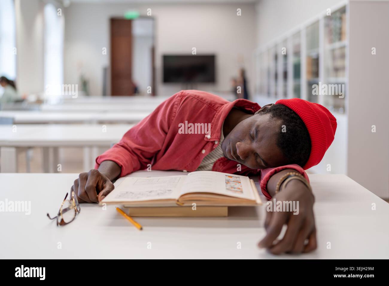 Tired exhausted African guy student falling asleep while studying in library Stock Photo