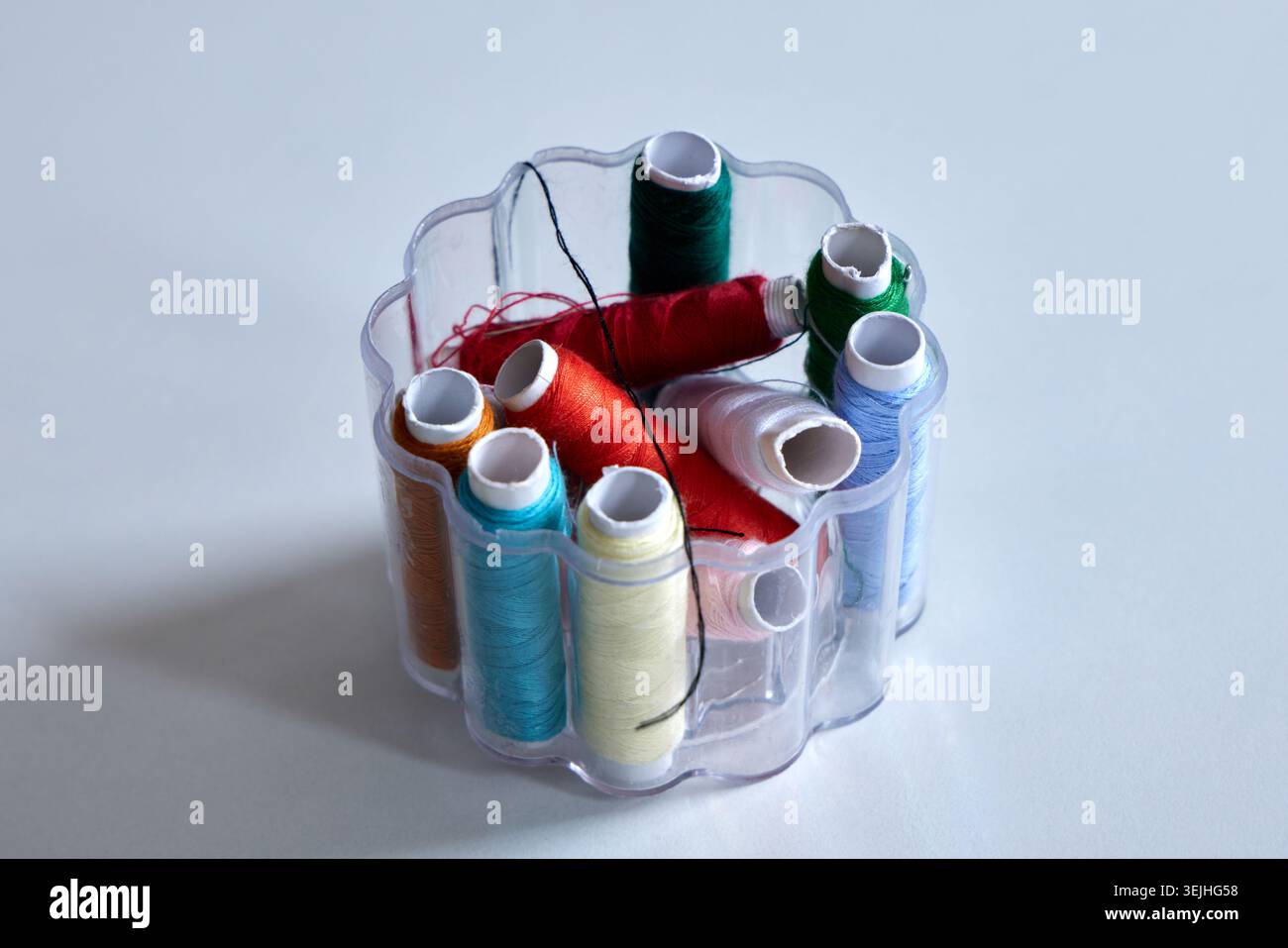 A plastic organizer box filled with various colorful sewing thread spools on a white surface. Stock Photo