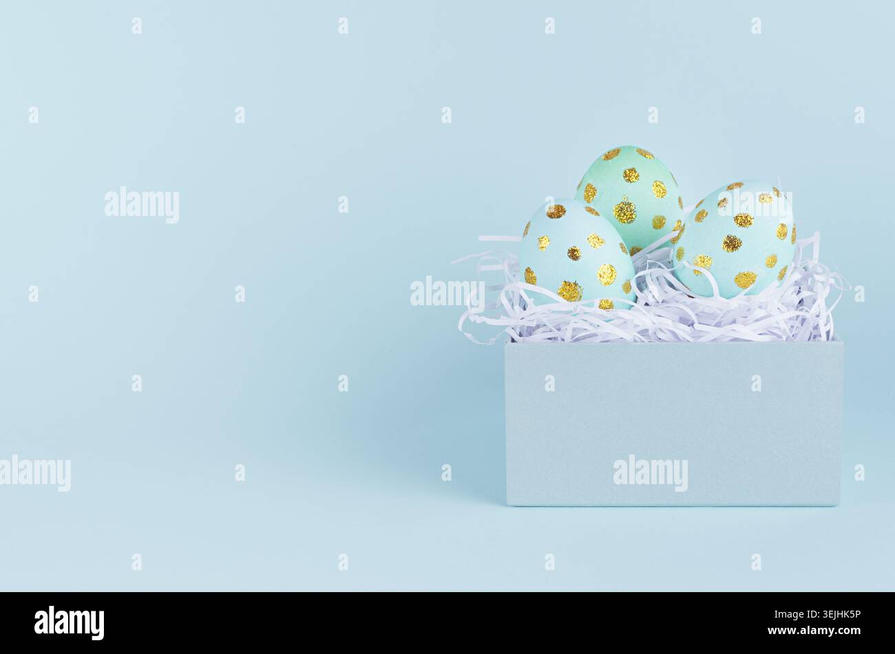 Simple and minimal easter background - easter eggs with golden dots in gift box on blue backdrop. Stock Photo