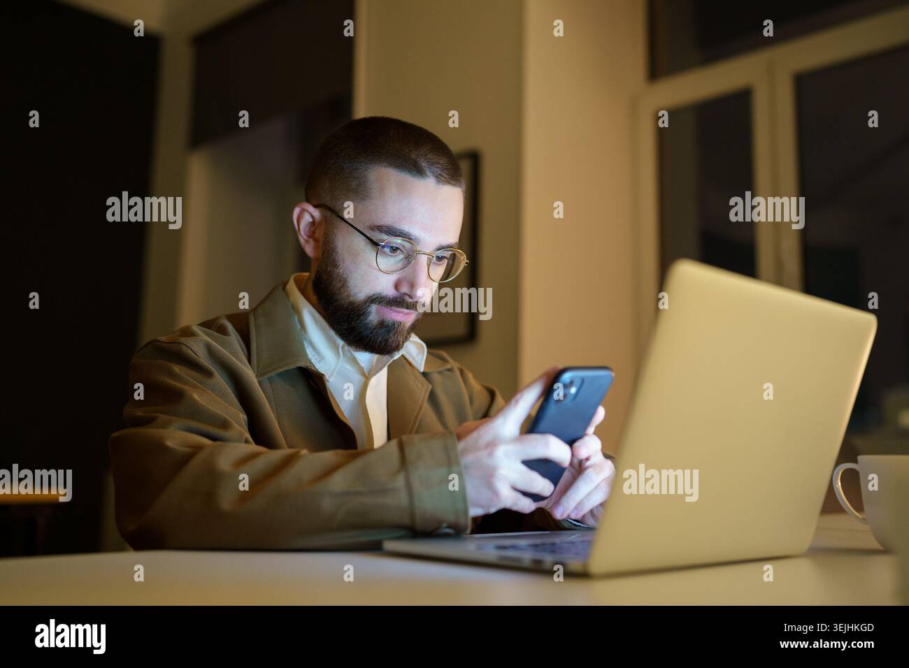 Focused young front end developer or qa engineer testing app on smartphone workloaded, work overtime in empty coworking space before project deadline. Stock Photo