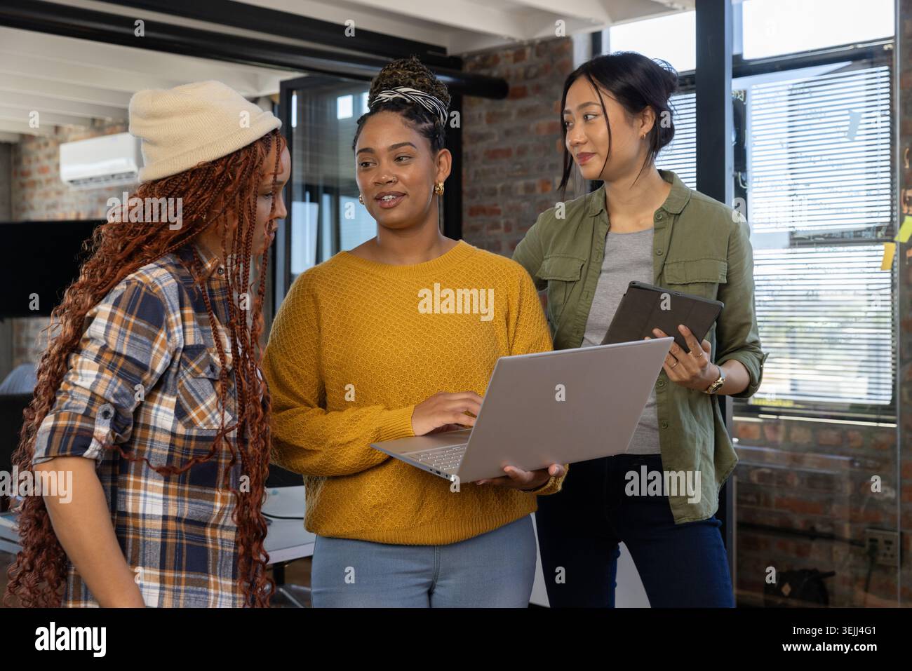 Diverse female coworkers collaborating while reviewing data on laptop and tablet in loft office. Collaboration, teamwork, modern Stock Photo