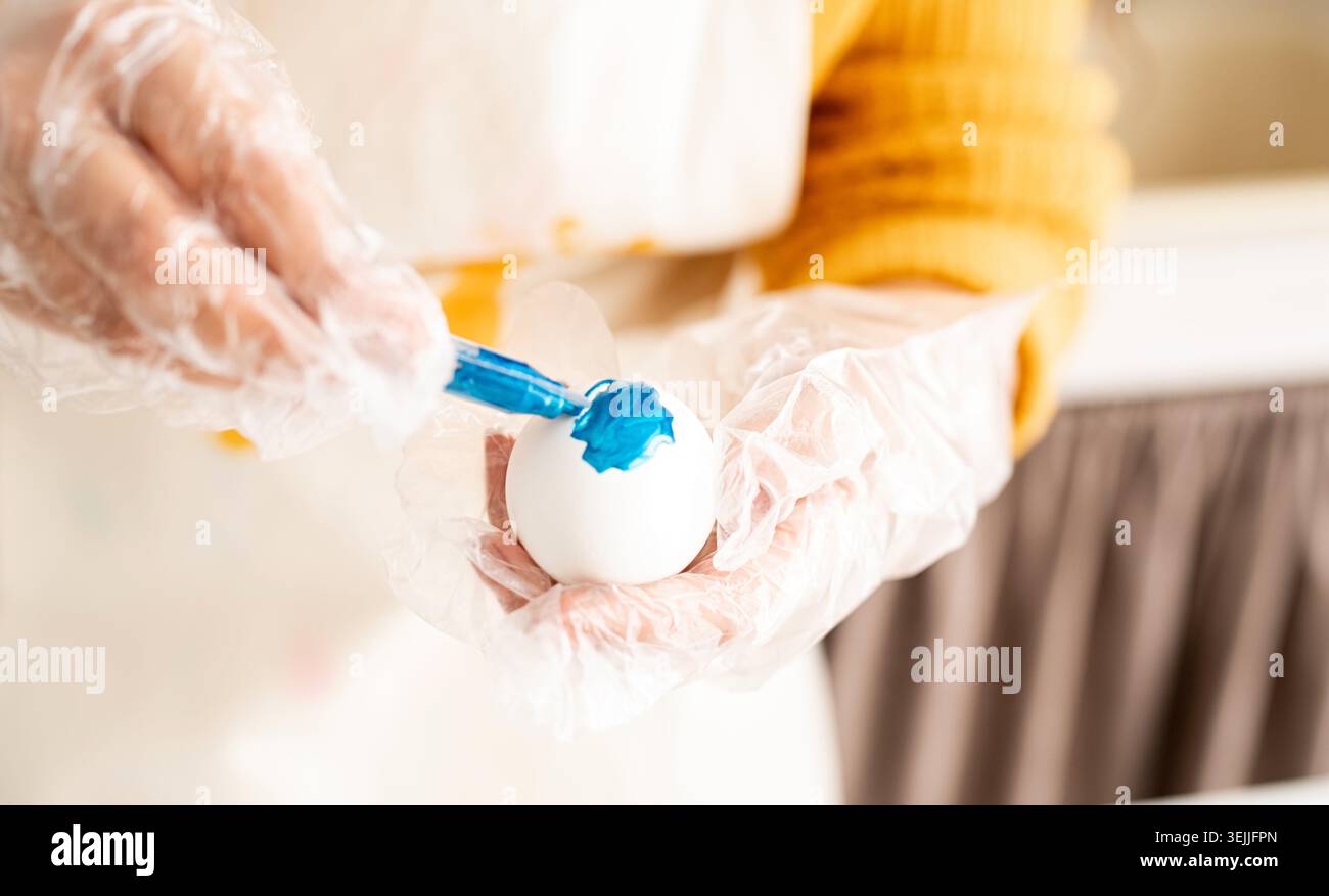 Close up of woman hands in gloves coloring easter eggs Stock Photo