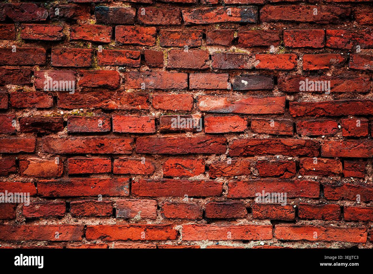 Red brick wall displaying cracked surfaces and worn mortar, creating a gritty texture Stock Photo