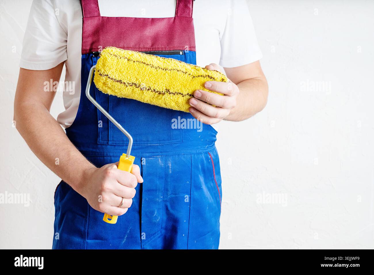 Closeup of a worker in blue overalls with a roller for coloring walls Stock Photo