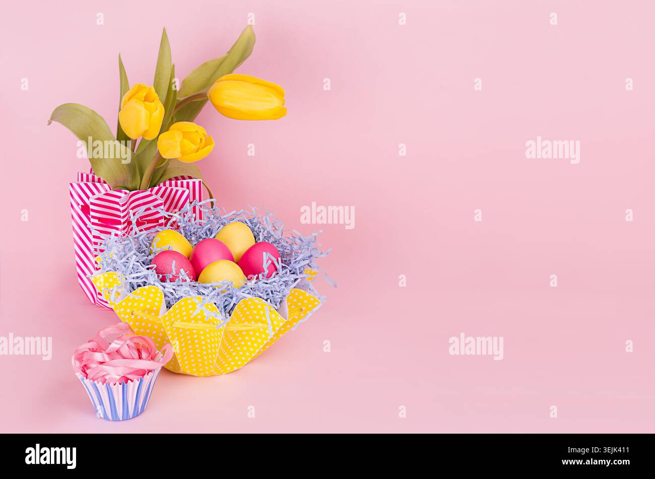 Springtime easter festive background - homemade painted multicolored eggs, tulips bouquet on pastel light pink background. Stock Photo