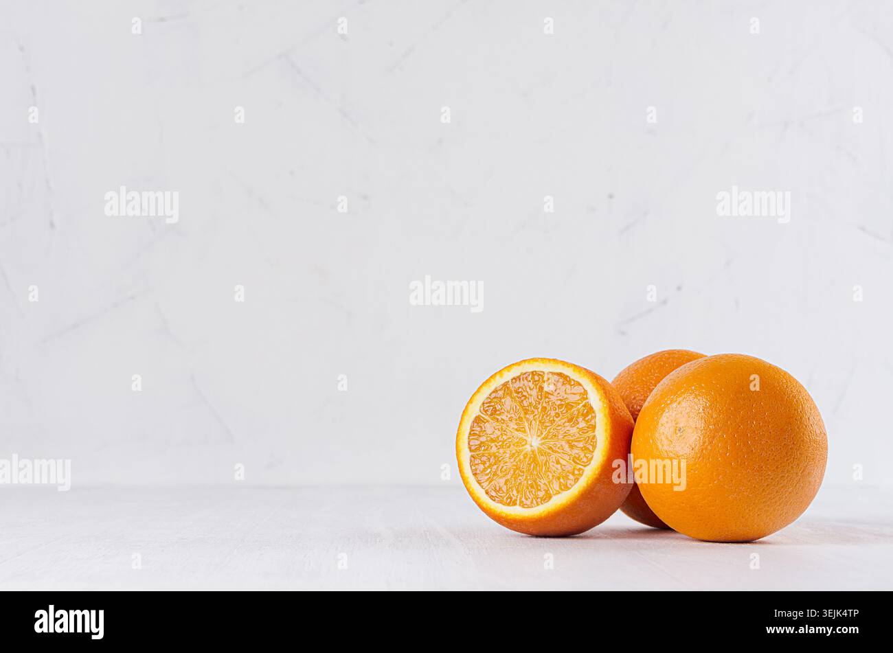 Three oranges and slice on white wood table and plaster background. Stock Photo