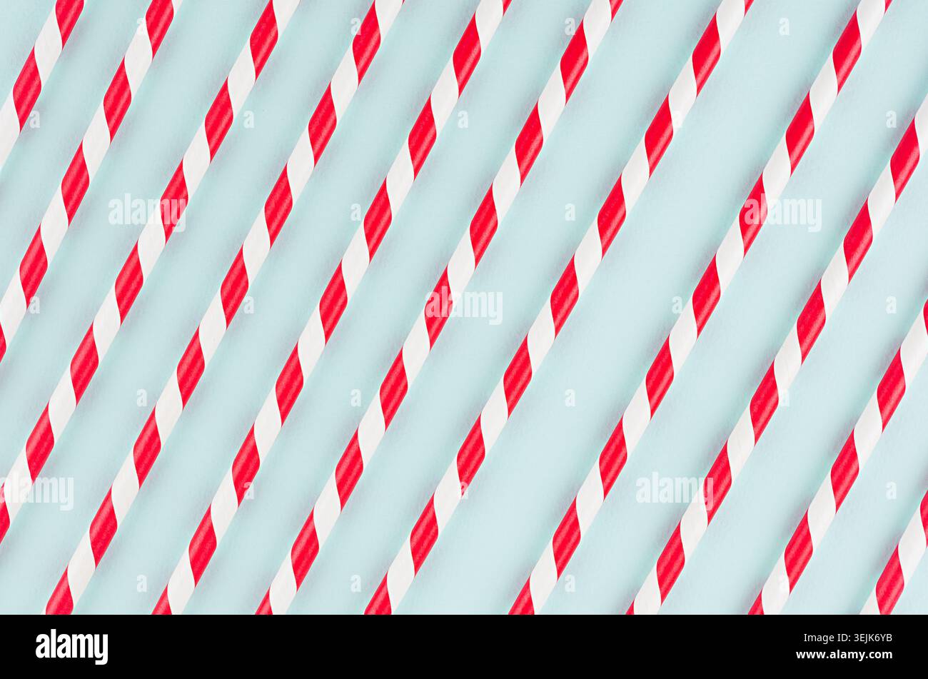 Red striped cocktail straws on pastel mint color as abstract joyful background, diagonal lines pattern. Stock Photo