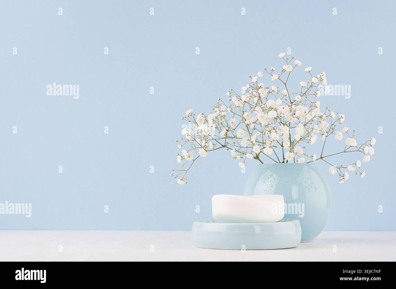 Bathroom interior - ceramic accessories - light blue circle vase, soap with white flowers on white wood table. Stock Photo