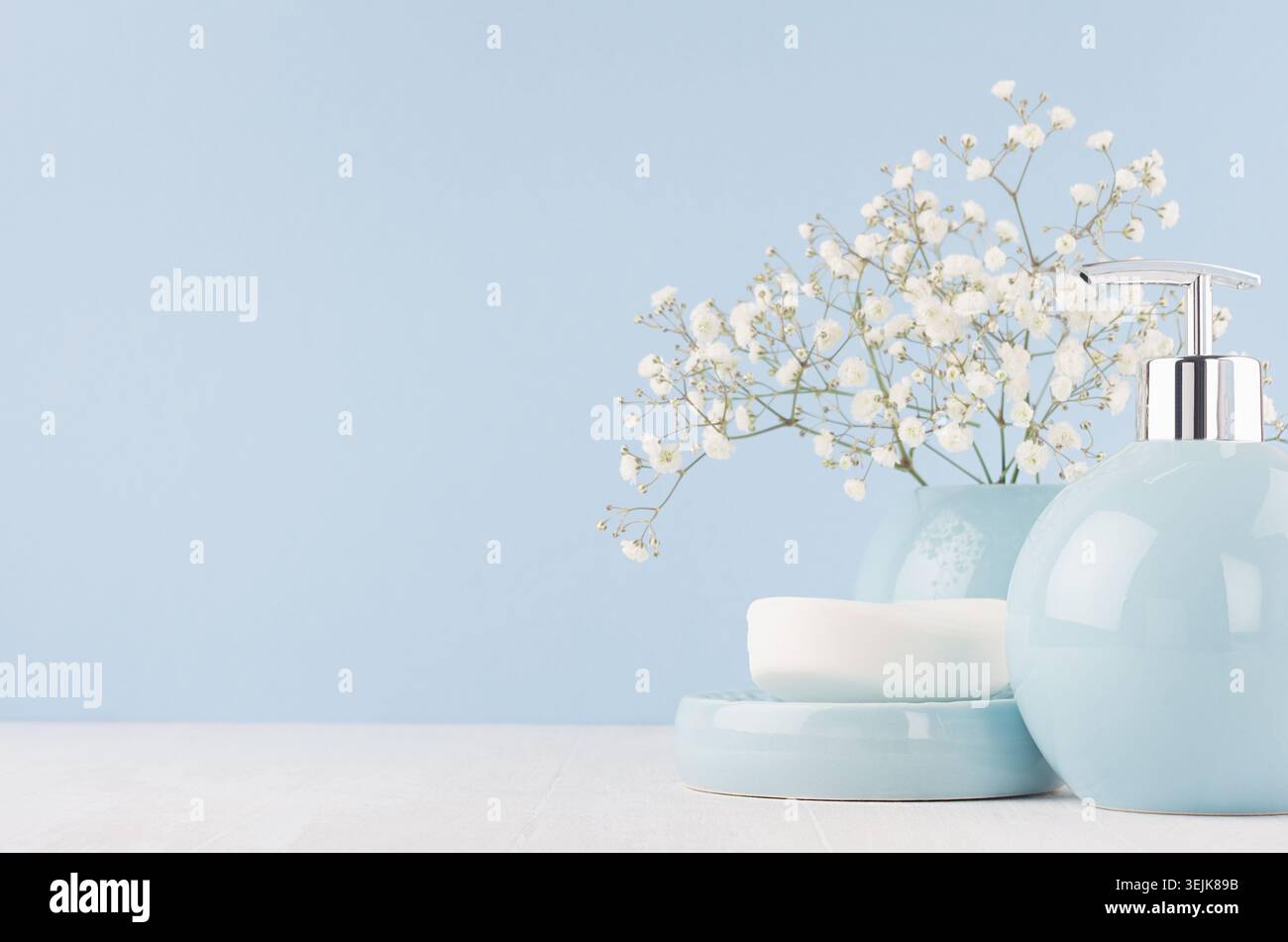 Bathroom interior - ceramic accessories - light blue circle vase with white flowers, soap dispenser on white wood table. Stock Photo