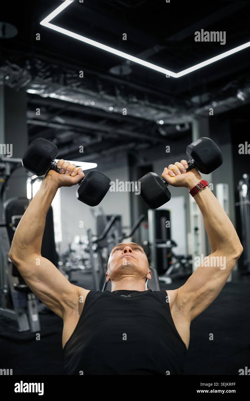 Strong man doing dumbbell bench press in gym Stock Photo