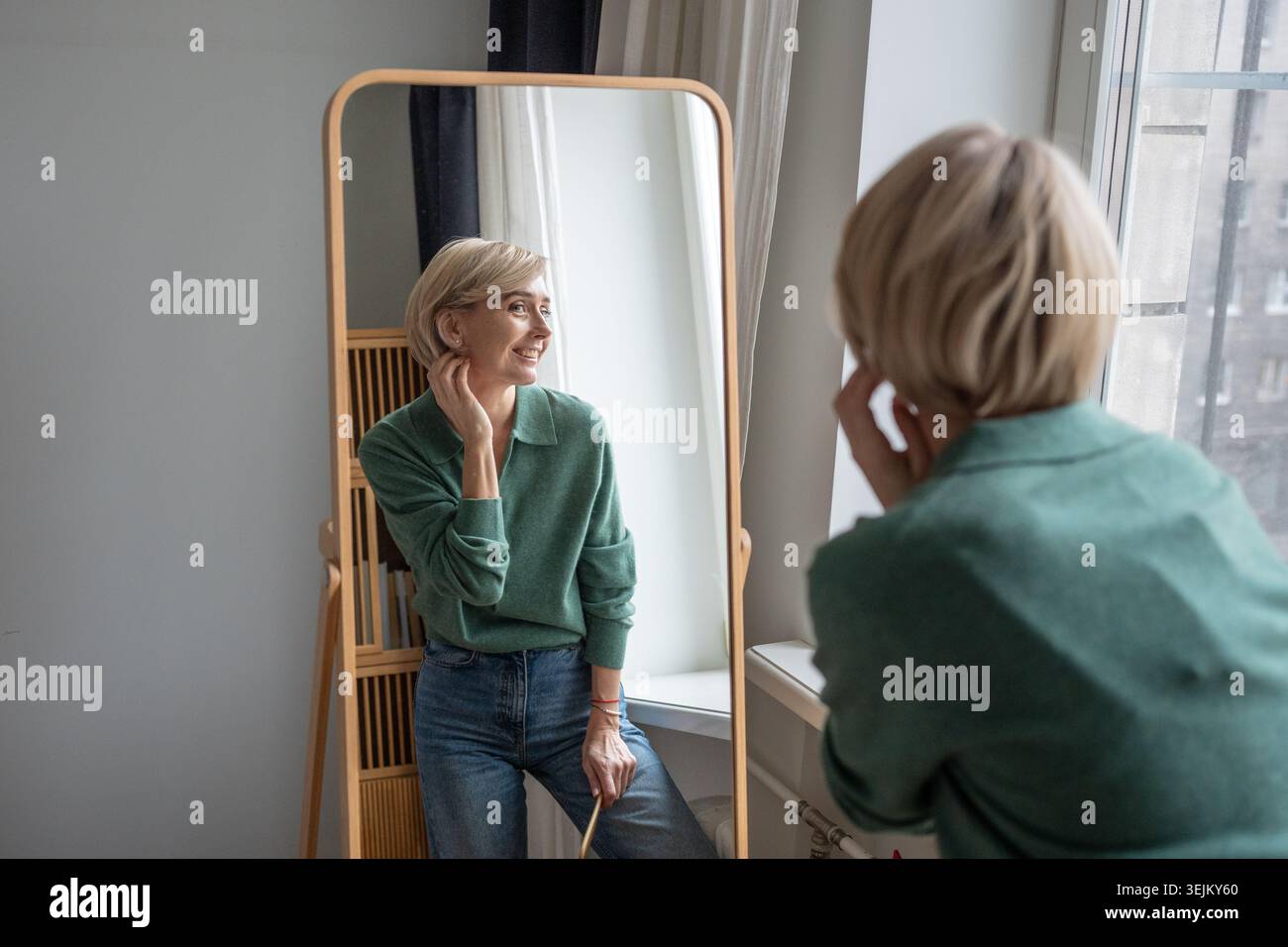 Joyful smiling woman appreciating own reflection in mirror, looking with positivity and confidence. Stock Photo