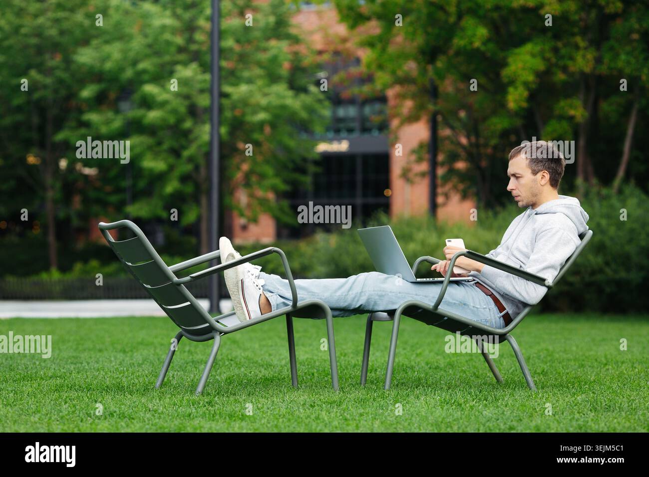 Millennial web developer work outside in urban park using laptop and smartphone. Distant workspace Stock Photo