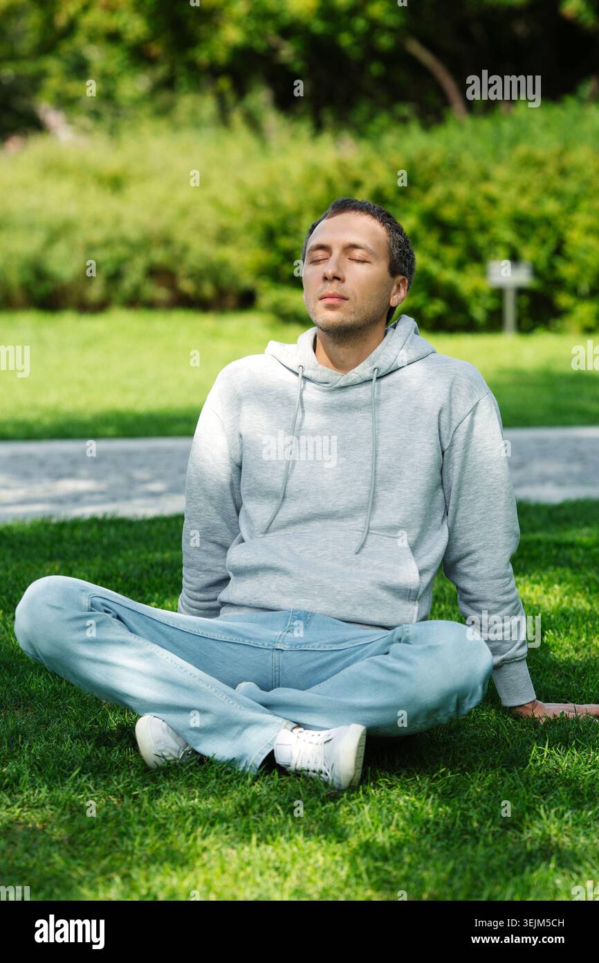 Freelancer man sitting on grass in park resting during break from work, relaxed, breathes fresh air Stock Photo