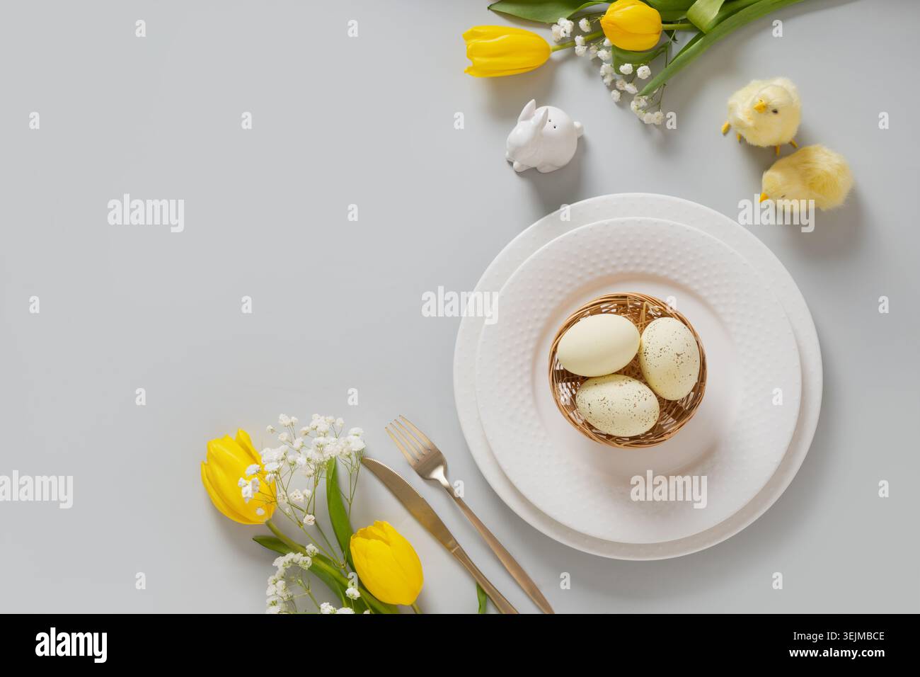 Easter table setting with yellow tulips, white plate, eggs and bunny. Stock Photo