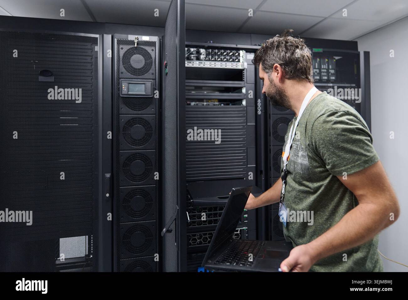 IT technician working on server rack in data center with laptop performing network maintenance Stock Photo