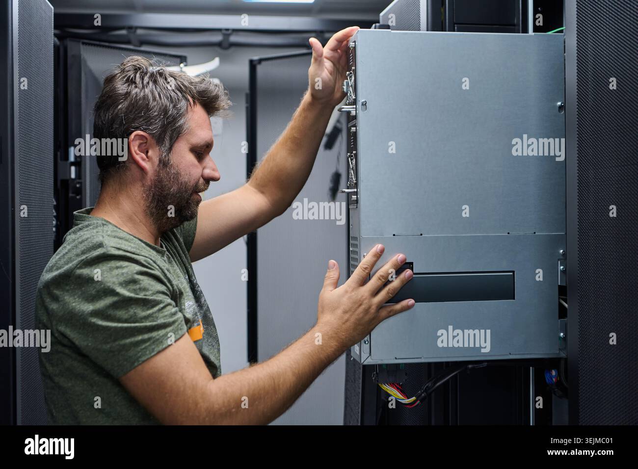 IT technician working inside a data center, installing and adjusting server hardware in a rack while performing maintenance, cable management and netw Stock Photo