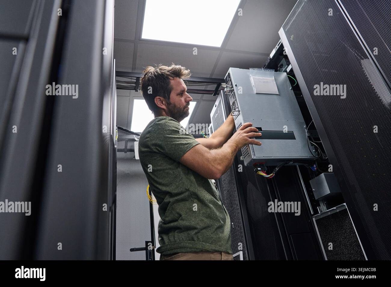 Data center technician installing server hardware and cabling in a server rack during maintenance work Stock Photo