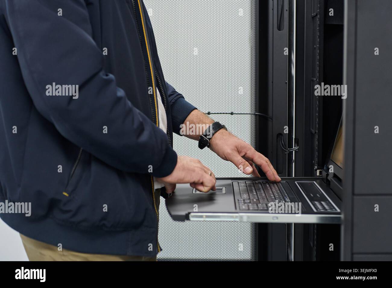 IT technician configuring a rack server using a slide-out console laptop in a data center Stock Photo