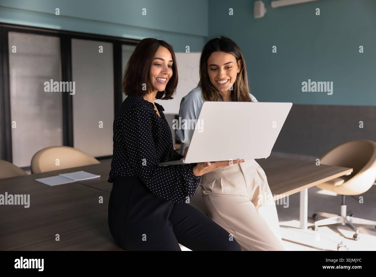 Two diverse women colleagues collaborating on laptop in office Stock Photo