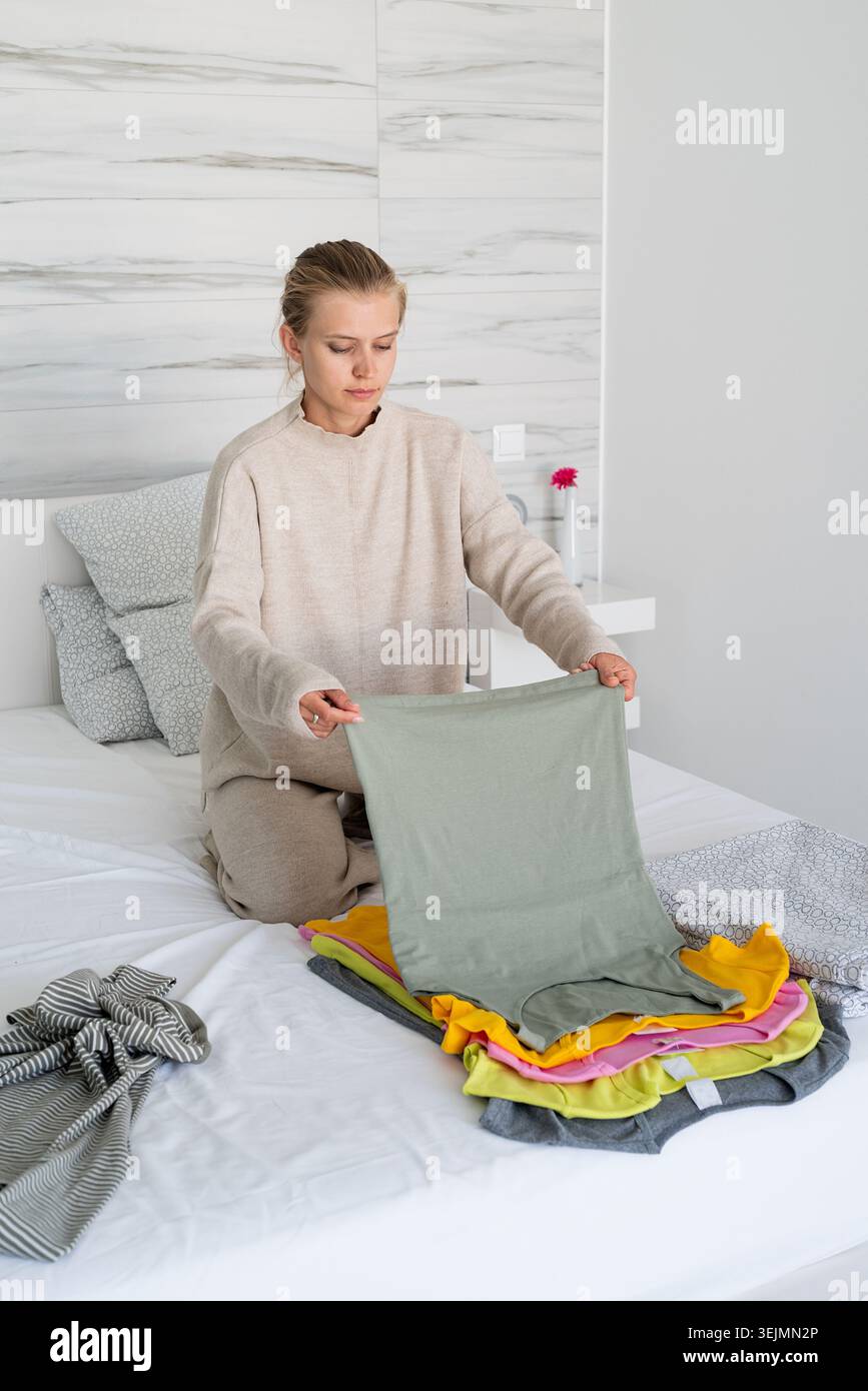 Young woman in comfy clothes arranging clothes sitting on the bed Stock Photo