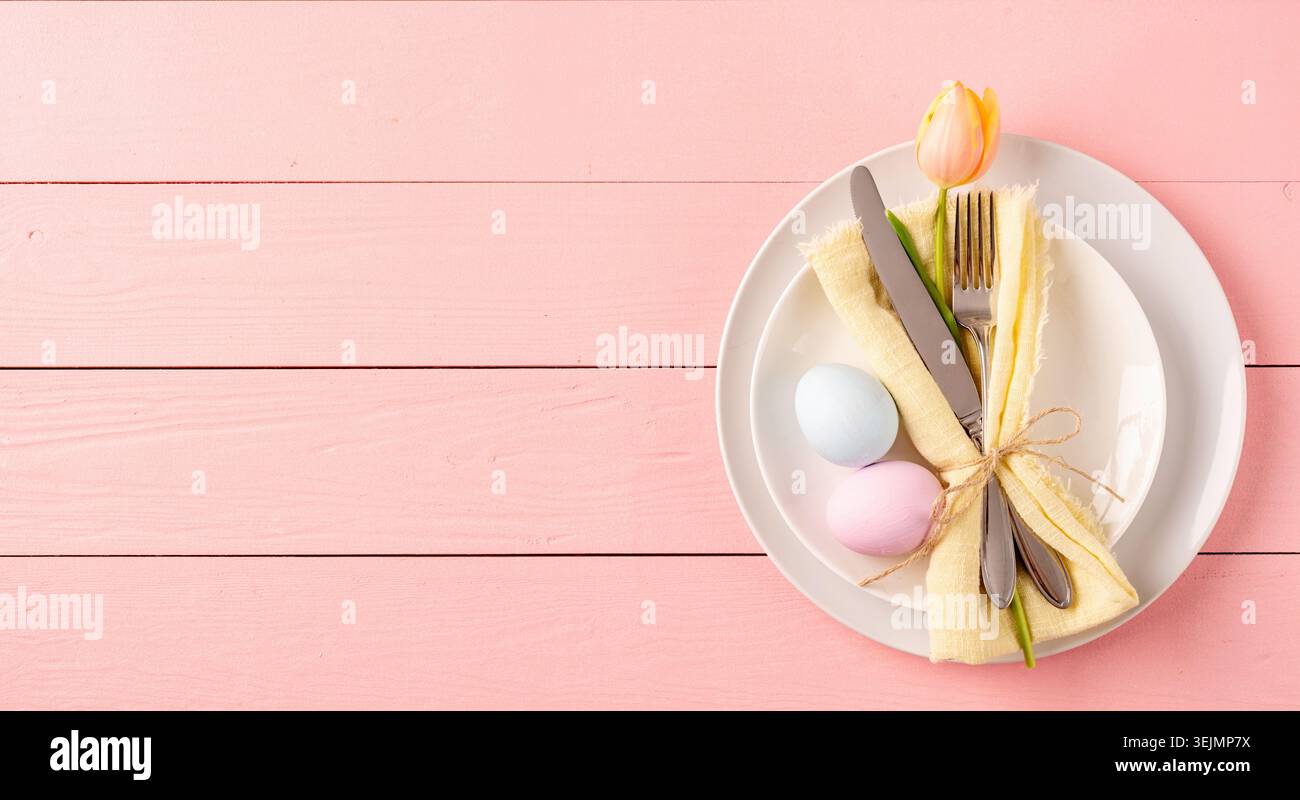 Table setting for Easter feast. Easter eggs, tulips and cutlery top view flat lay on pink rustic background Stock Photo