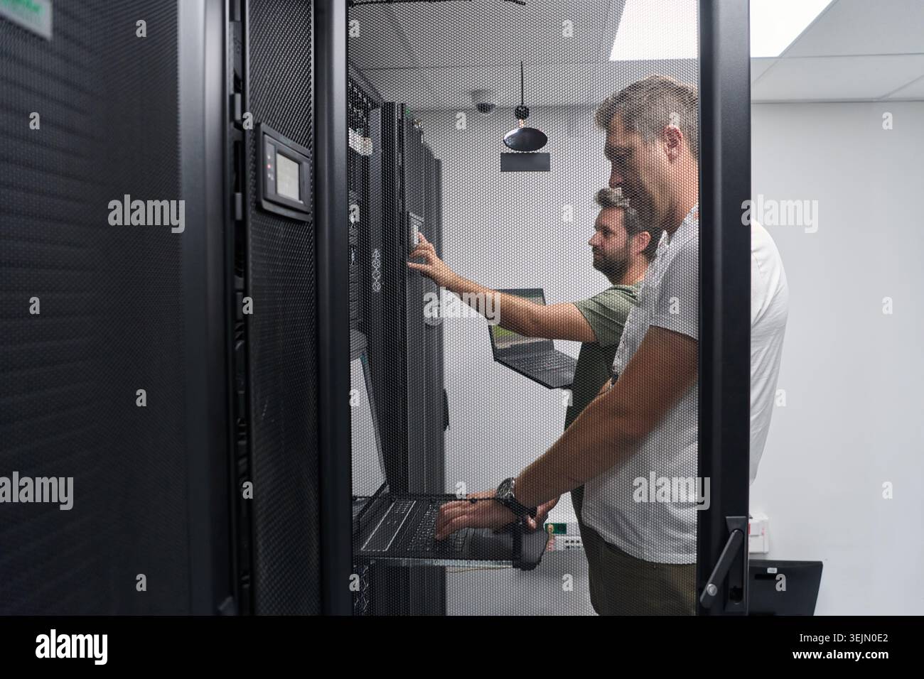 Two IT technicians working on servers in a data center performing network maintenance and system checks Stock Photo