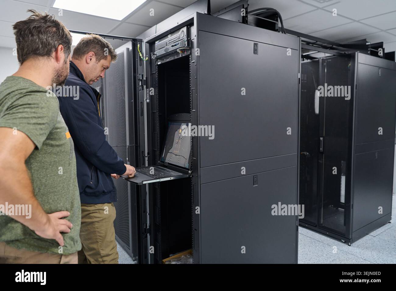 Two IT technicians working on a server rack with a laptop in a modern data center Stock Photo