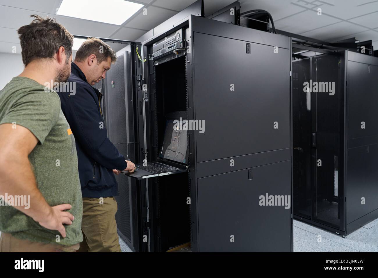 Data center technicians troubleshoot rack-mounted servers using a pull-out console laptop during maintenance Stock Photo