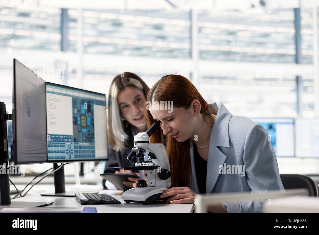 Engineering team analyzing nanotechnology circuits with microscope in microchip factory RD office, brainstorming. Teamworking colleagues inspect PCB parts with optical gear in research facility Stock Photo
