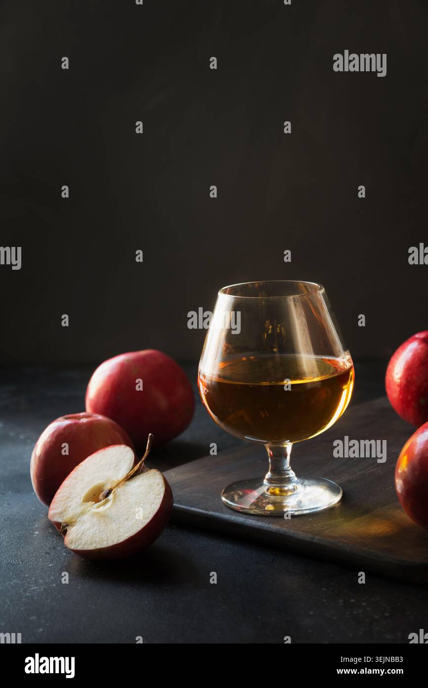 Glass with Calvados brandy and red apples on black. Stock Photo