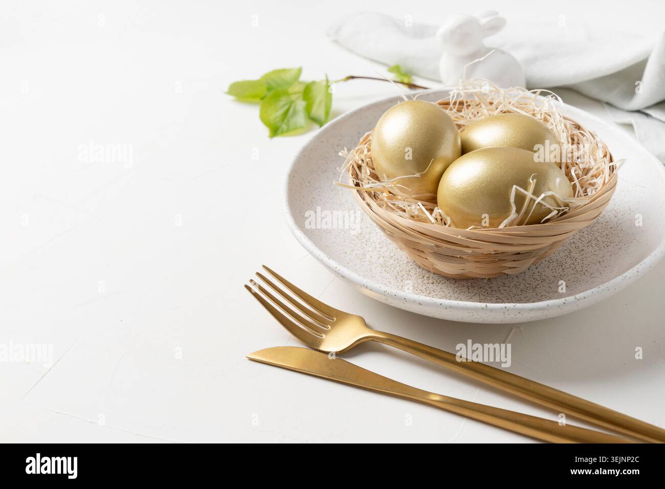 Easter table setting with bunny and golden eggs on white table. Close up. Stock Photo