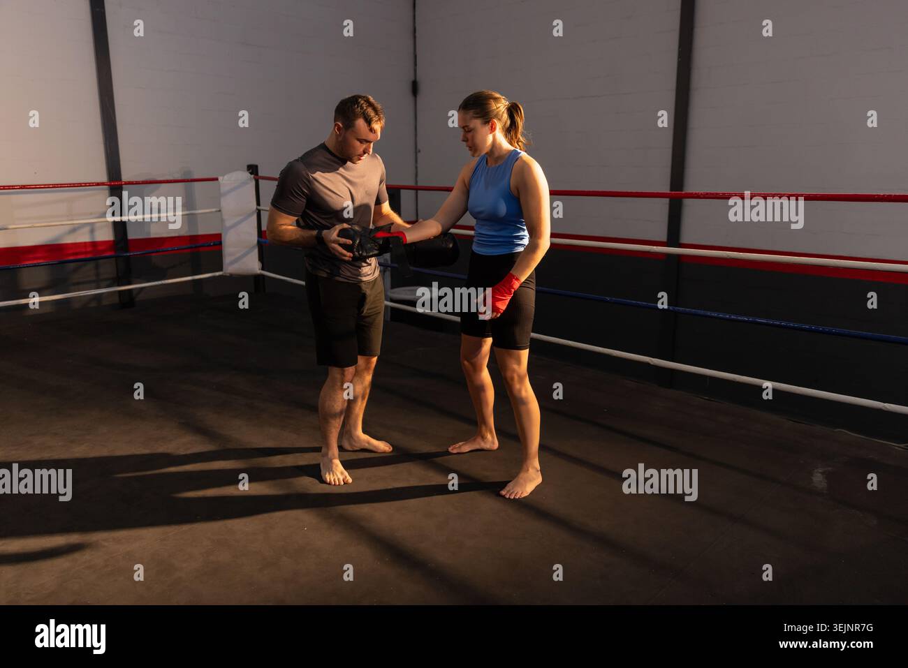 Trainer and boxer practicing punches holding focus mitts, wearing red hand wraps in boxing ring. Coach, fighter, training, gym, Stock Photo